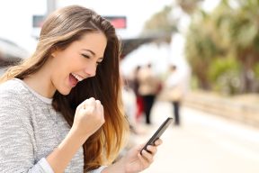 Euphoric woman watching her smart phone in a train station while is waiting